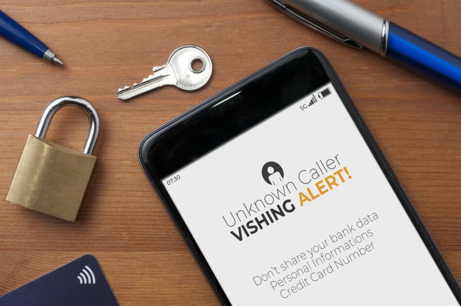 The phone screen displays an incoming call with an unknown number. A bright red banner flashes across the screen: "Vishing Alert!" Below it, a clear message warns: "Don't share bank details, personal info, or credit card numbers!"